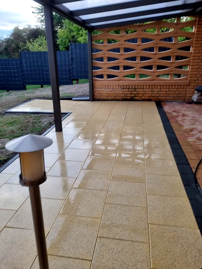 Überdachte Terrasse mit hellen Platten und Gartenleuchte